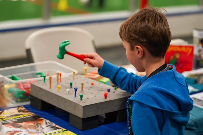 A young student plays with a toy hammer on an activity board on one of the tables at the event