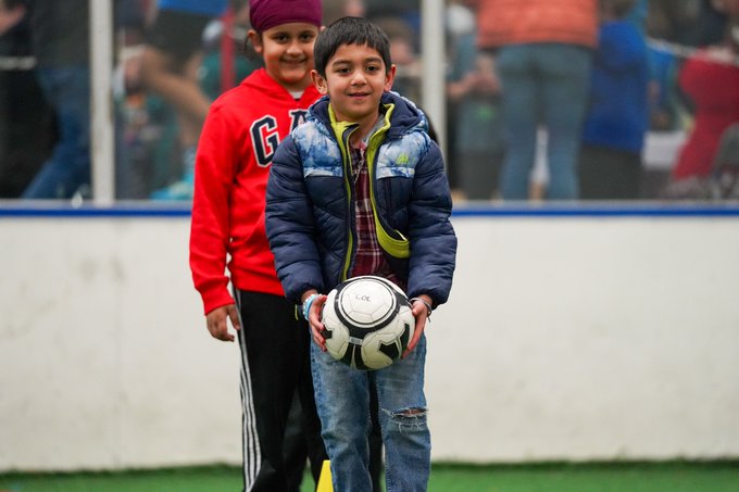 A student smiles and prepares to drop kick a soccer ball on the indoor soccer field