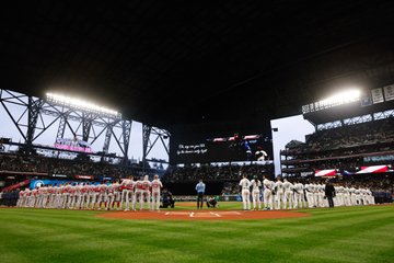 Wide-shot of both teams standing on the field during the national anthem. 