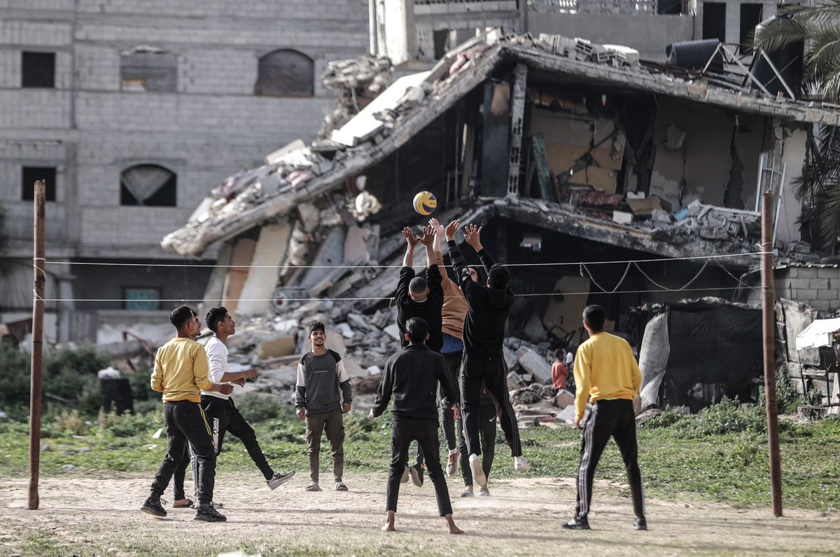 Palestinian youths, who take refuge in Nuseirat camp from ongoing Israeli attacks, pass the time by playing volleyball near a partially collapsed building while waiting for iftar time on the Holy month of Ramadan in Gaza . (Photo by Ali Jadallah/Anadolu via Getty Images)