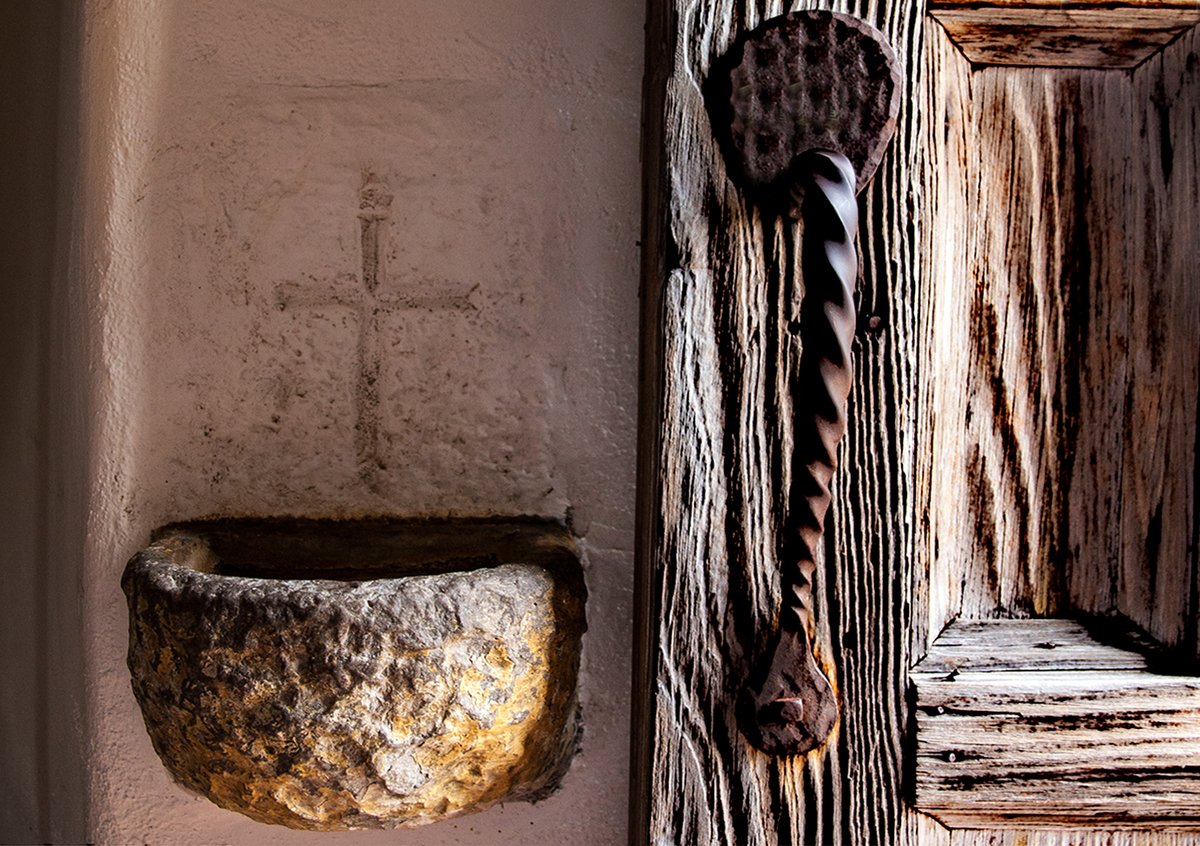 An opened door and the holy water stoup at the entrance to the church at Mission Espada in San Antonio. I don't know how old the stoup is but it looks like it's been there awhile. The church was completed in 1756, so ... One of my own photos, taken in 2009.