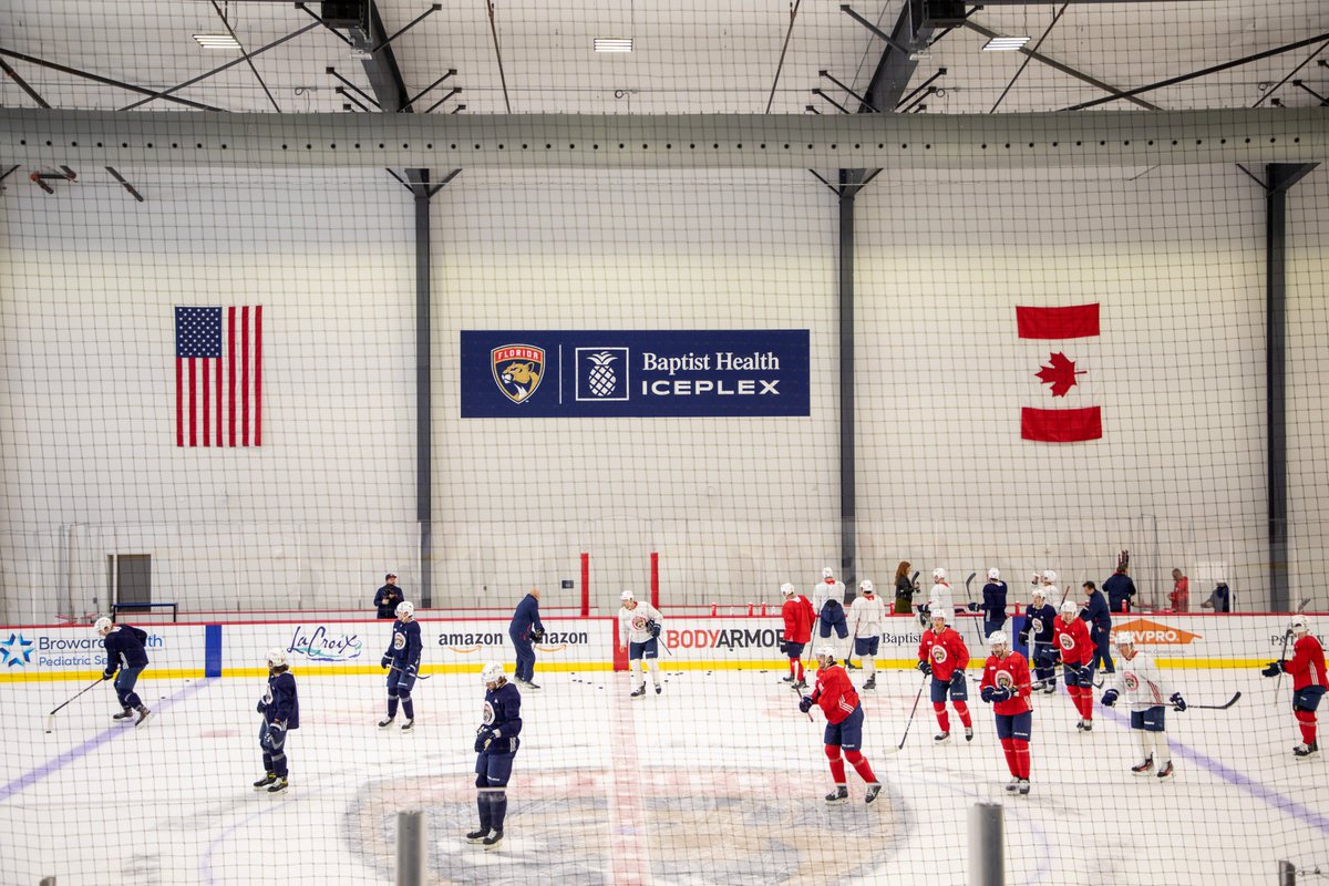Florida Panthers' players skate on the Baptist Health Rink. On the wall is a navy sign with white font that says: "Baptist Health IcePlex"