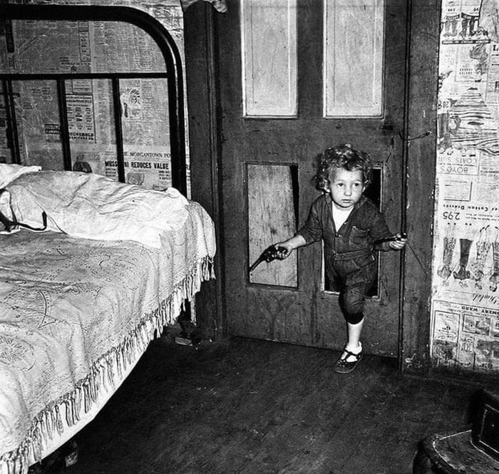 El hijo de un minero de carbón usa un agujero en la puerta para entrar a un dormitorio con una pipa en una mano y una pistola en la otra en Bertha Hill, Virginia Occidental. Foto de Marion Post Wolcott, 1938.