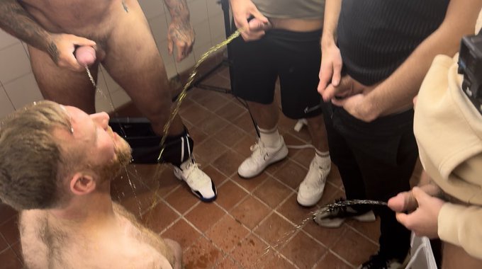 6 horny lads piss all over their mate in the gym locker room. He gets a hot golden shower from 6 lads