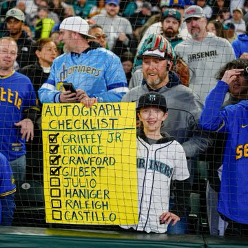 Photo of a Mariners fan holding up a sign: AUTOGRAPH CHECKLIST: GRIFFEY JR. FRANCE CRAWFORD GILBERT JULIO HANIGER RALEIGH CASTILLO