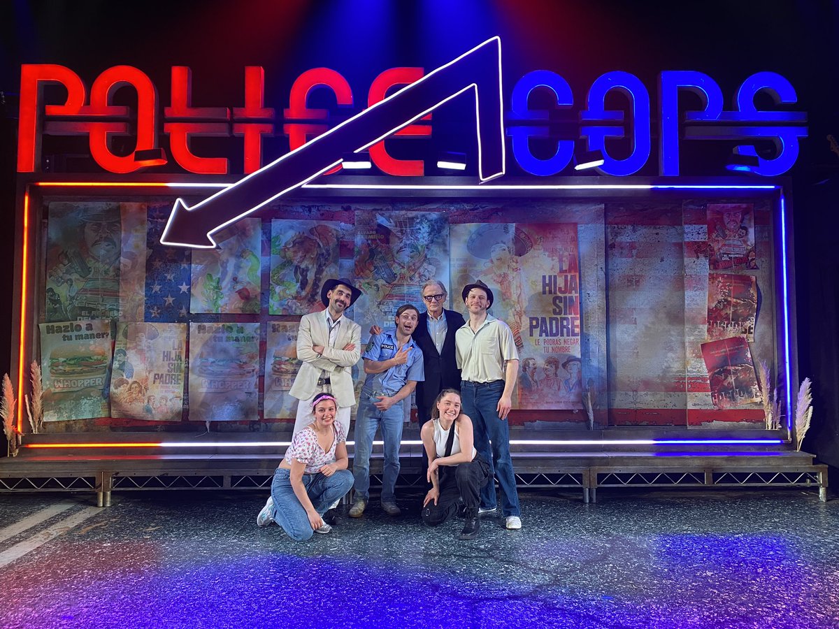 Bill Nighy smiling and posing with the cast of Police Cops onstage.