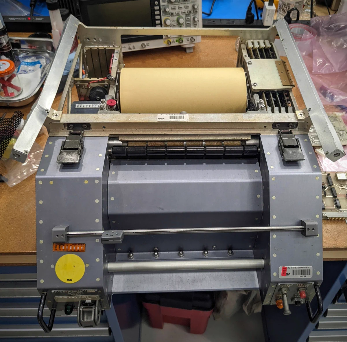 The teleprinter is a gray metal unit. It has a roll of brown paper at the back. There are a few lights and switches on the front.