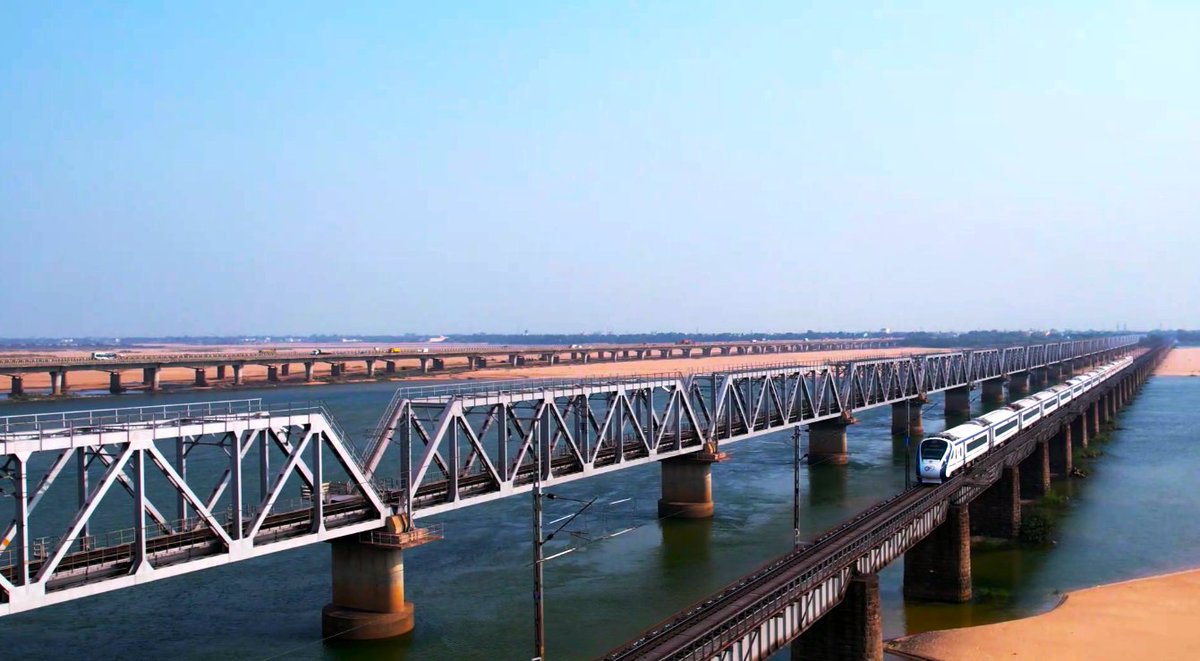 Under the sunny azure sky, the #VandeBharatExpress gracefully traverses the Rail Bridge spanning the majestic Mahanadi River in Cuttack, Odisha.