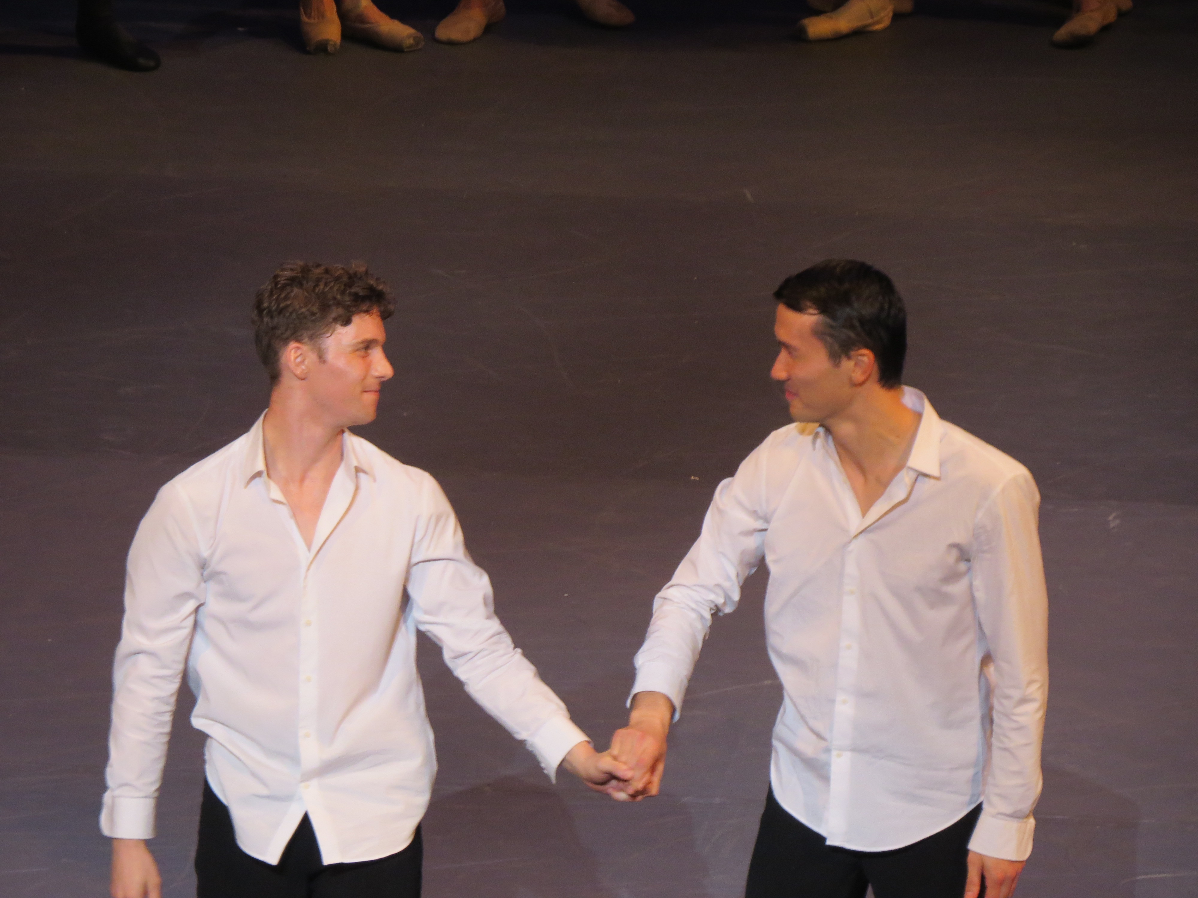 Dancers Travis Clausen-Knight and James Pett  in white shirts black trousers holding hands as they take a bow.