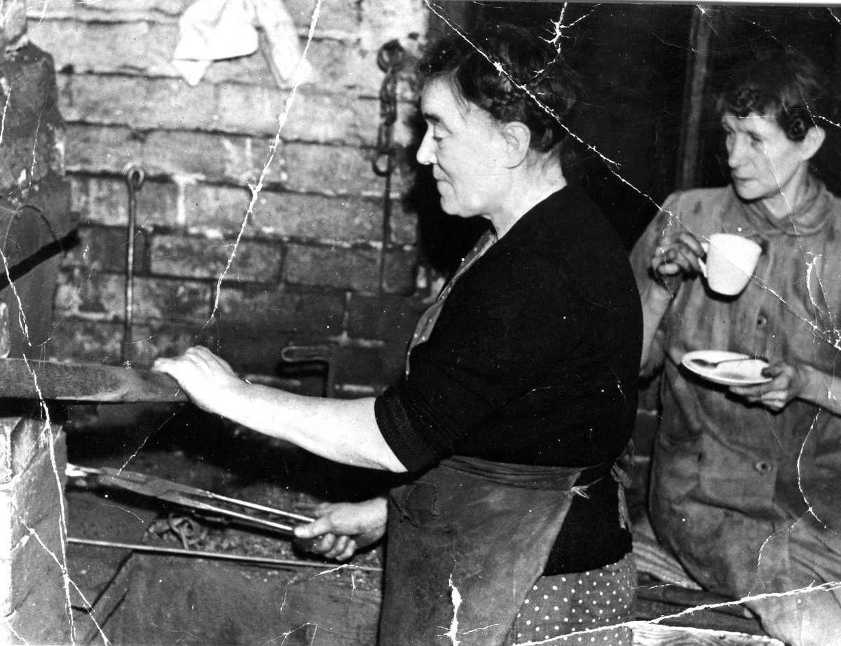 Think it's time for a cuppa tay, ay it ☕ Photo: BCLM Collection - a lady chainmaker works at the furnace as her colleague stops for a cup of tea.