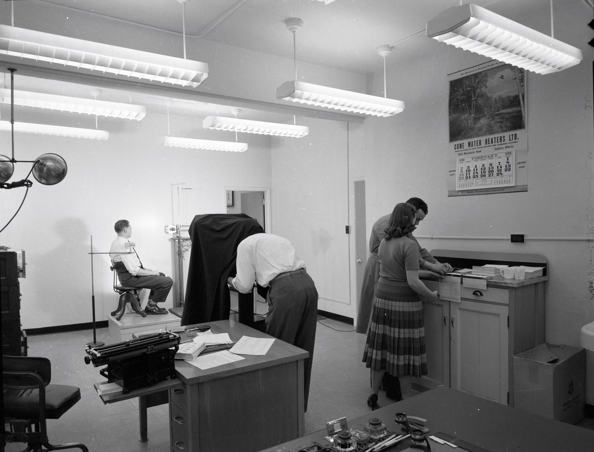 This #FlashbackFriday, we take a look at what the Identification office looked like on a typical workday in 1958. In the photo, you see Detective Don Nelson fingerprinting a woman while Detective Irv Loewen is using the studio camera to take a mugshot. #CalgaryHistory #yyc