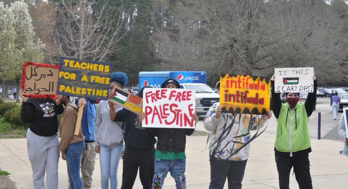 Photo: a group of students protest outside of a school, holding signs that say "teachers for a free palestine," "free free palestine," "intifada intifada," and "Is this scary DPS?"