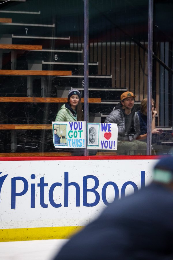 Fan holding signs with Bjorkstrand meme and Larsson bowlcut photo on them