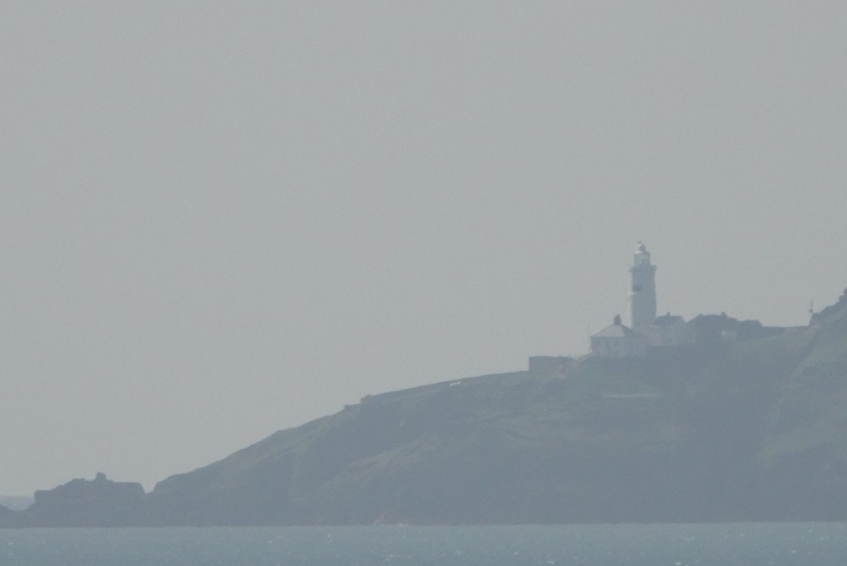 A distant, hazy view of Start Point lighthouse from nine miles away on the coast path near Kingswear, Devon today.