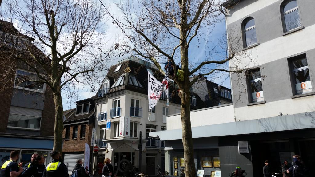 In Grevenbroich ist am Gericht wenig, dafür auf dem Marktplatz etwas los. Zwei Aktivist*innen sind auf die Bäume geklettert und hängen ein Transparent auf. #CiaoGrevenbroich