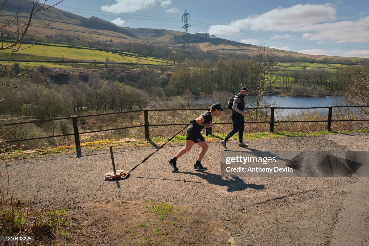 Ben Eastwood, a mental health coach from BeOne, looks-on as William Mahaffey pulls a 45kg weight around Valehouse Reservoir while training for a channel swim later in the year in High Peak, Derbyshire, England. (2021)