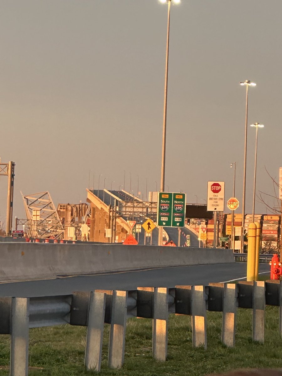 Scene from one side of the collapsed bridge in Baltimore. You can clearly see the on-ramp to the Bridge snapped off, the shipping containers on the cargo ship to the right and to the left, zoom in, the top of a red truck still stuck in the mangled remains ⁦@Channel4News⁩