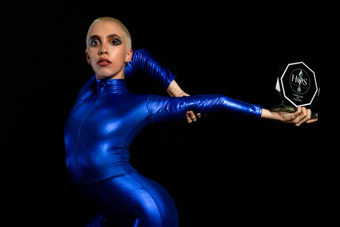 A dancer wearing a blue suit from House of Suarez stretching their arm behind them.