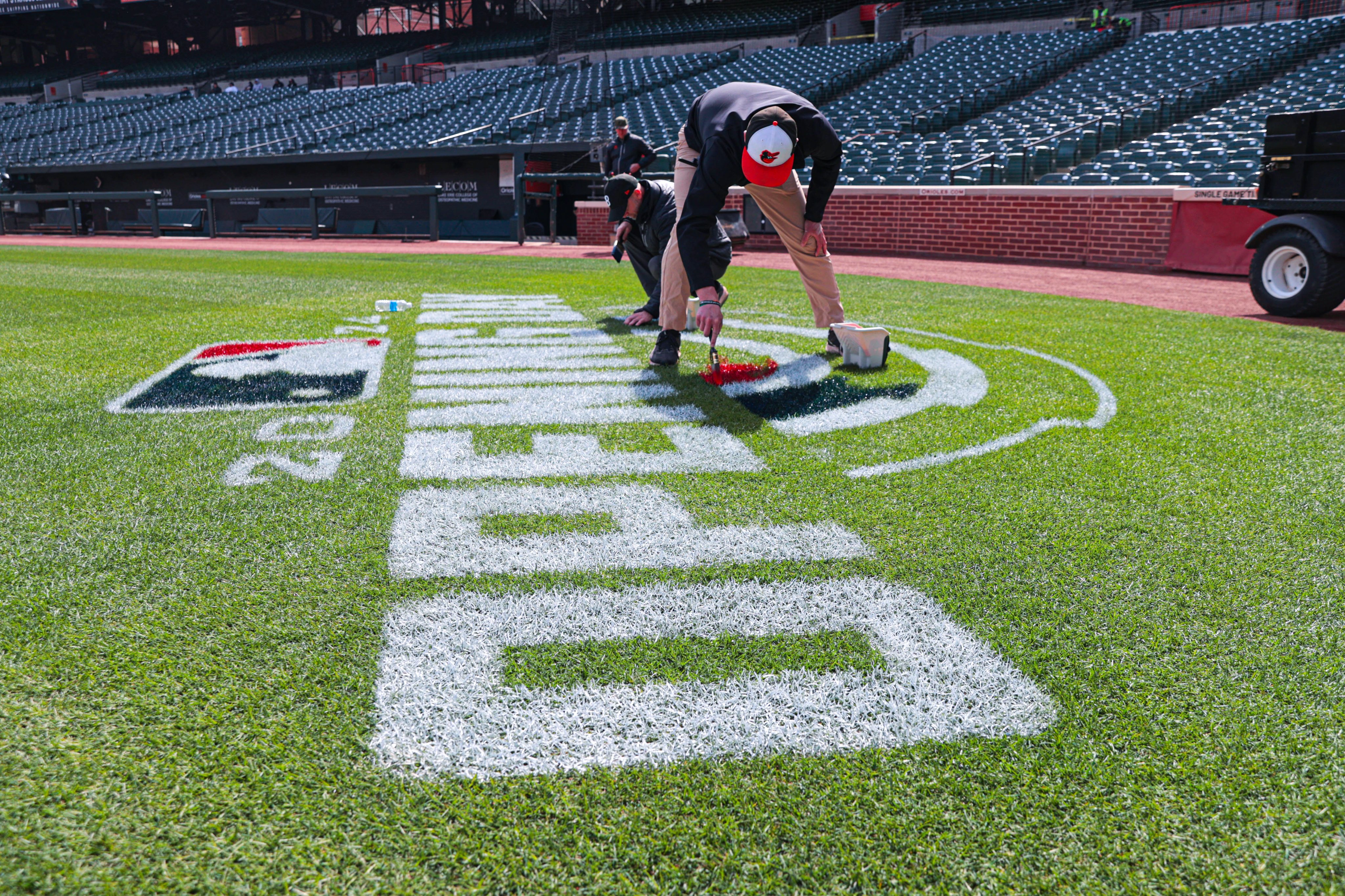 Grounds Crew members painting the Opening Day logo on the grass.