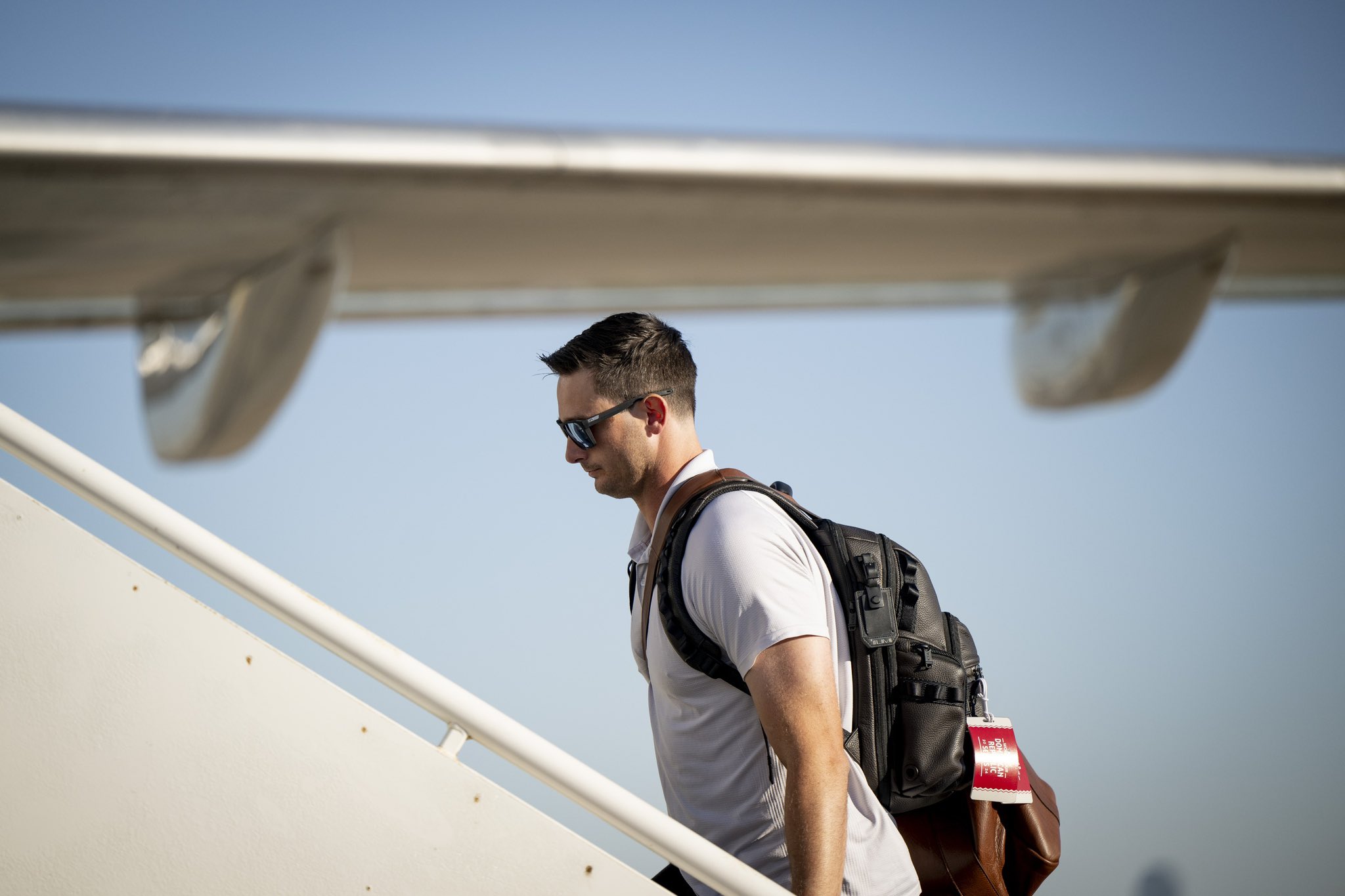 Garrett Whitlock wears a backpack and sunglasses as he walks up the stairs to the team plane to fly to Seattle.