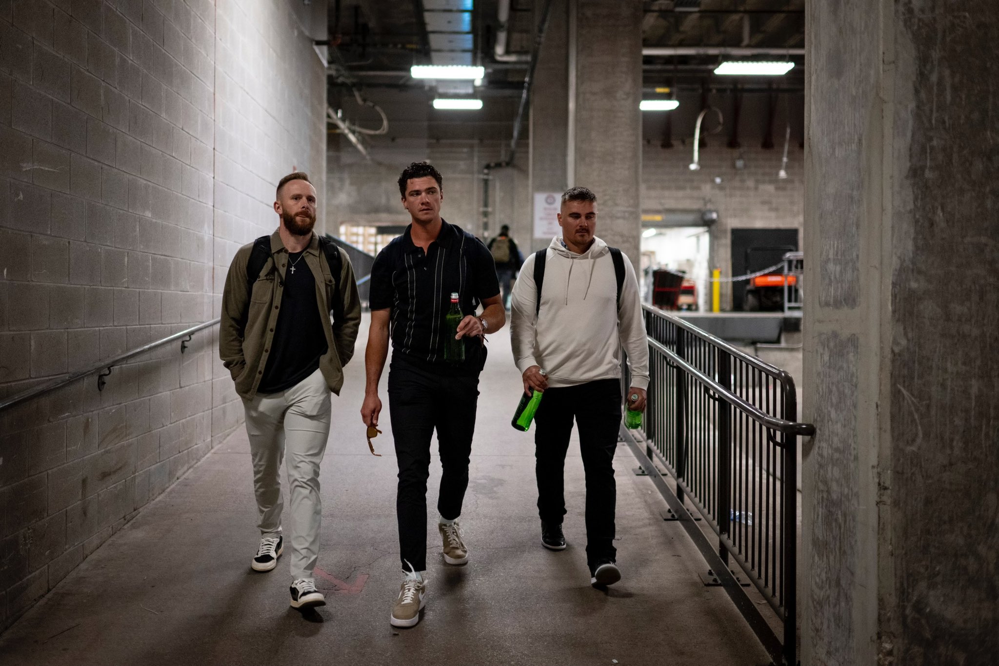 Trevor Story, Bobby Dalbec, and Reese McGuire walk down a ramp in casual clothes to catch the team bus on their way to the airport.