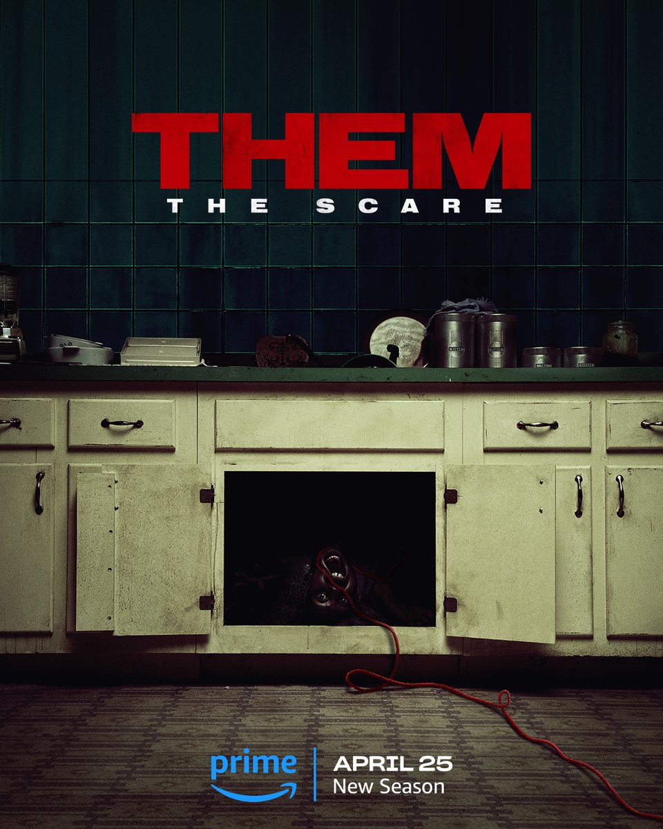A dingy kitchen with dark blue streaky tiles above a messy counter and sink full of dirty dishes, appliances, and pans. Beneath the counter are well-used drawers and cabinets, with the large cabinet below the sink wide open to reveal a person lying on their back, face contorted in a wide-mouthed scream as a thick red strand of yarn extends from their body out of the cabinet, curling over a grimy linoleum floor. Text on the tile backdrop read "THEM" in large bold red font over "The Scare" in smaller white font. On the bottom of the image are the Prime Video logo and the text "April 25," "Watch Now," and "New Season."