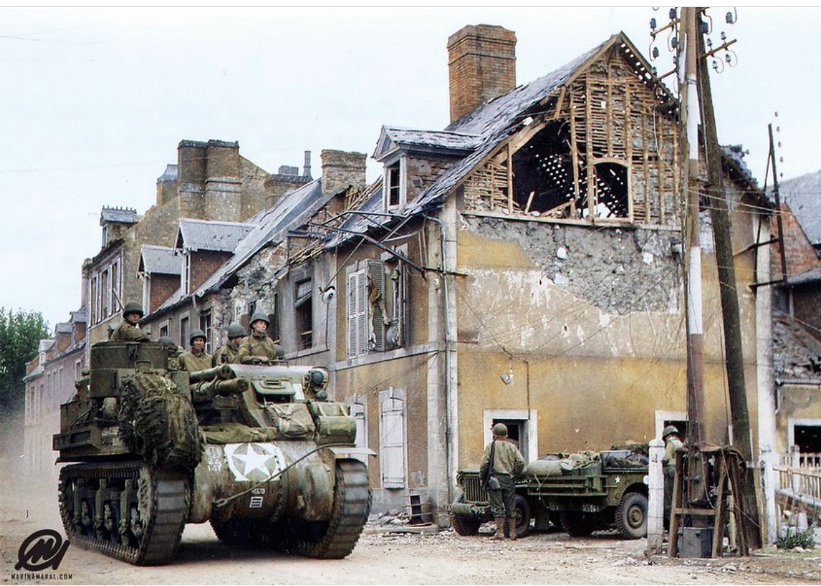 In June of 1944, an M7 Priest of the 2nd Armored Division moves through the intersection of Holgate Street & the Paris-Cherbourg railway in Carentan. 🪖 @marinamaral2 on the colorization 🎨