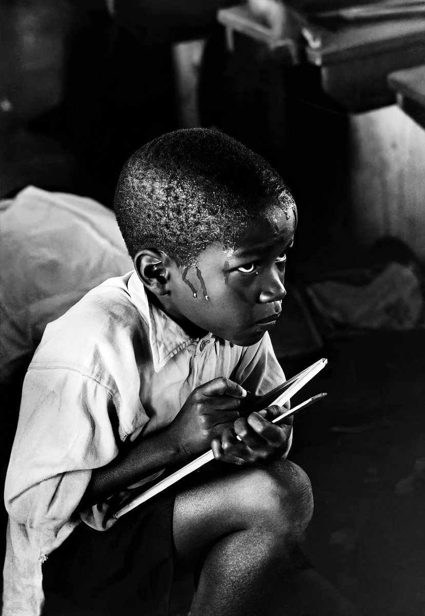 Ernest Cole - Earnest boy squats on hauches & strains to follow lesson in heat of parked classroom - South Africa - 1966