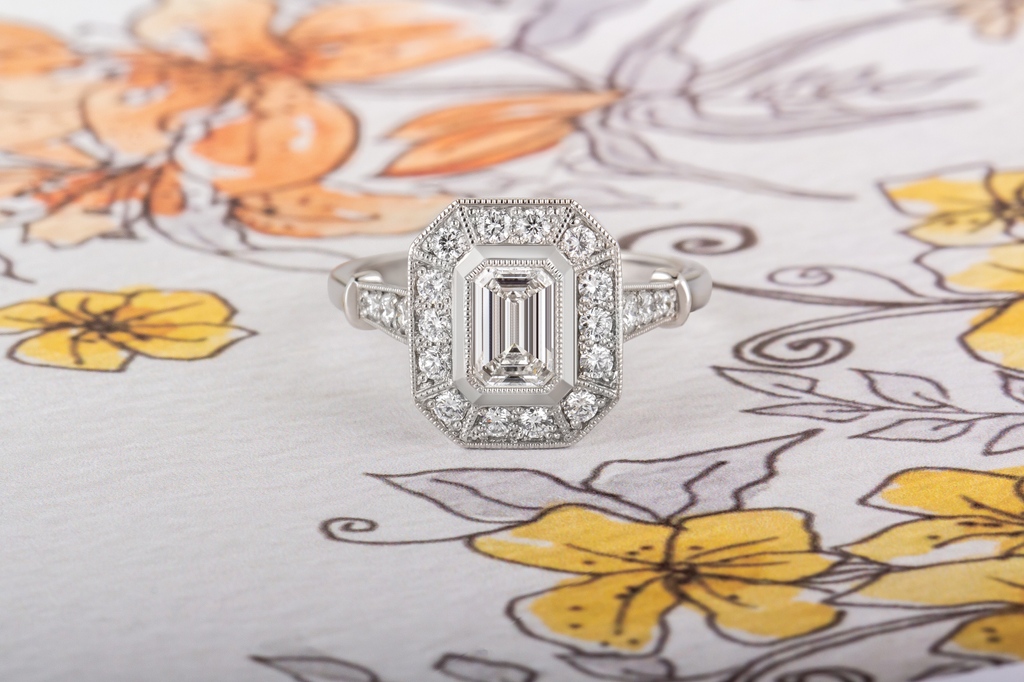 Be transported to the dramatic styles of the Art Deco era with this stunning Emerald Cut Diamond Halo Cluster Engagement Ring. A fine millegrain edging of small beads of platinum completes the vintage design of this beautiful engagement ring.