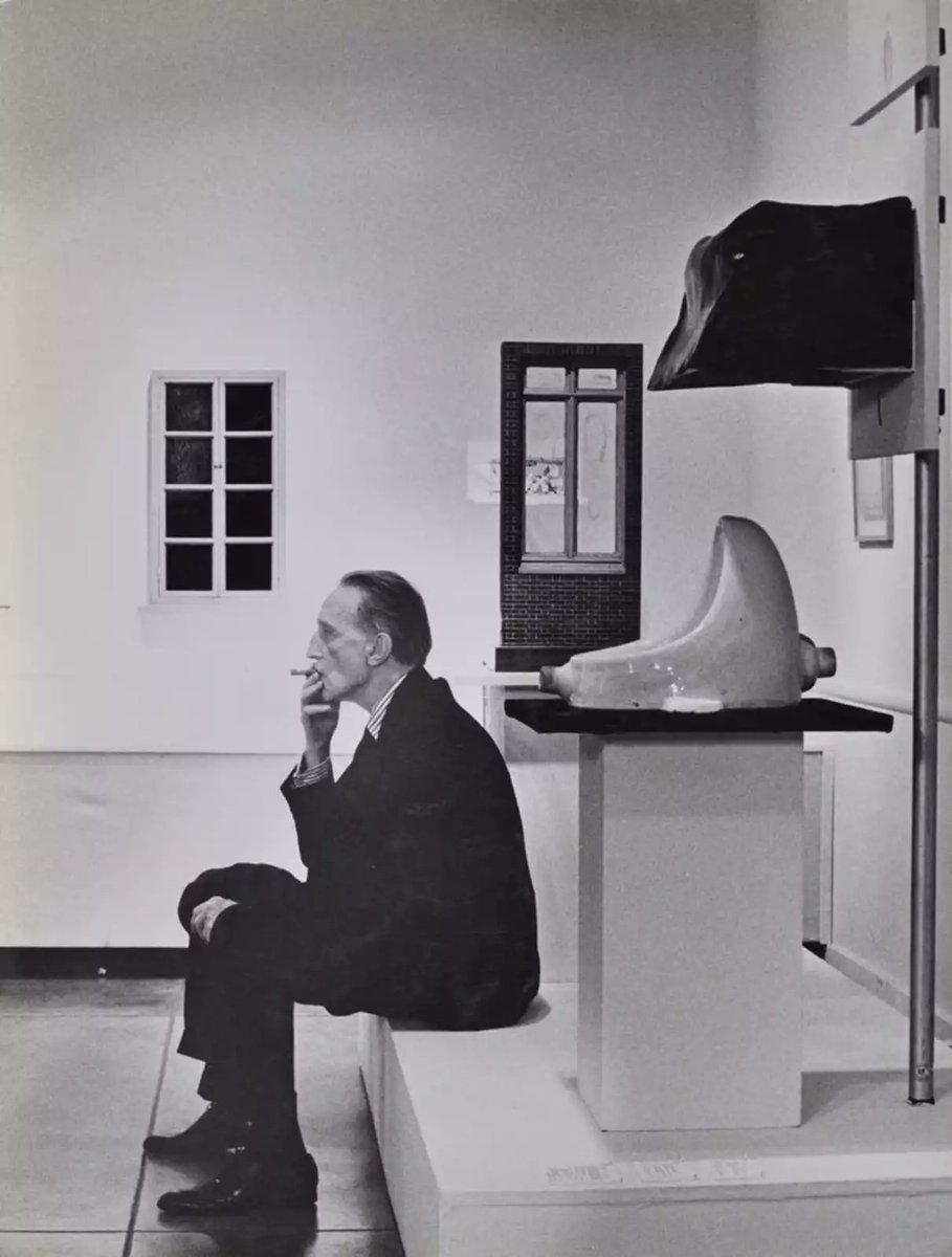 Duchamp smoking in front of Fountain, Duchamp Retrospective, Pasadena Art Museum, 1963 • Julian Wasser •