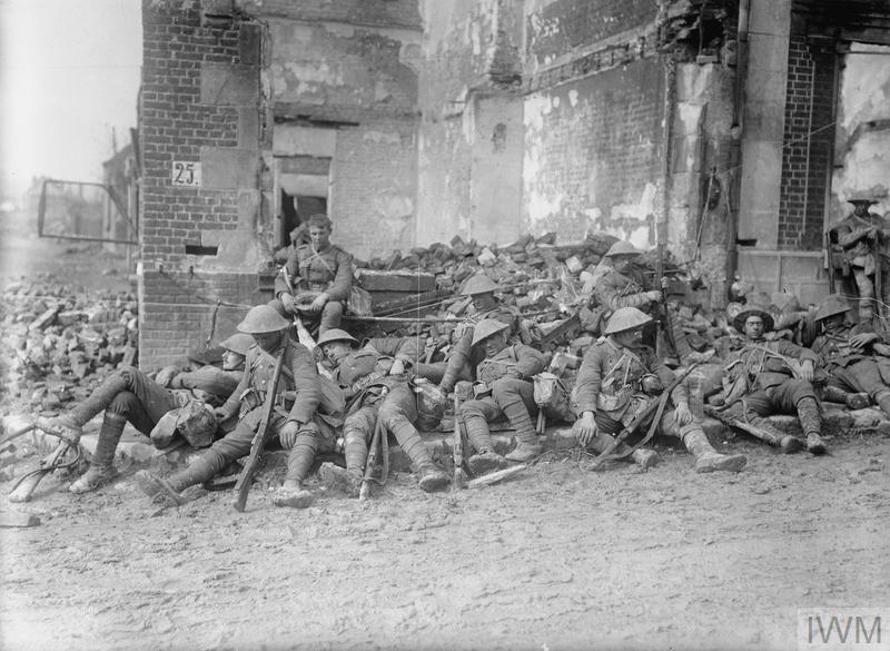 Party of British troops resting by a wrecked building in Athies, April 1917. IWM Q 1980