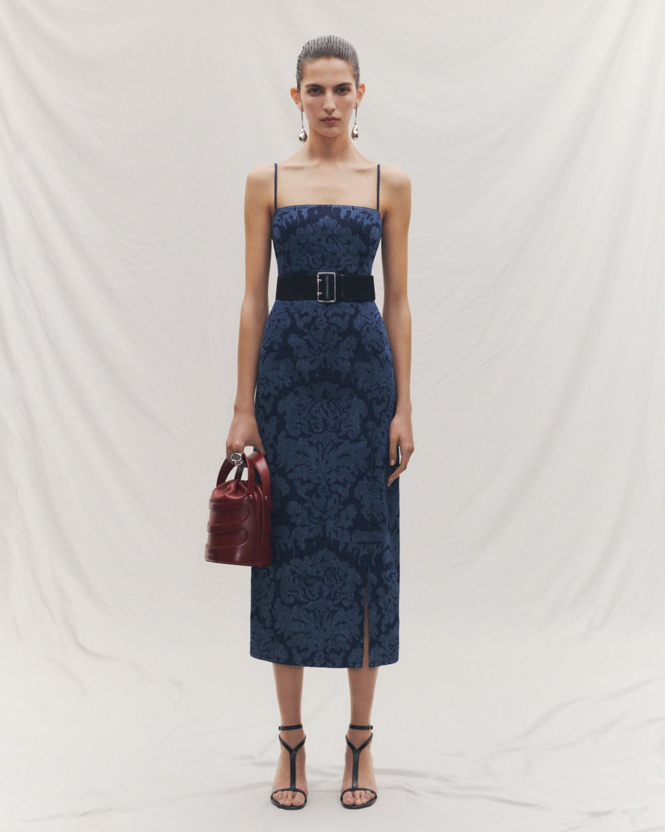 An indigo denim pencil dress featuring a damask jacquard, worn with a black waist belt, silver pearl Stick earrings and the Rise bag. Discover #McQueenSS24: on.alexandermcqueen.com/SS24_TW
