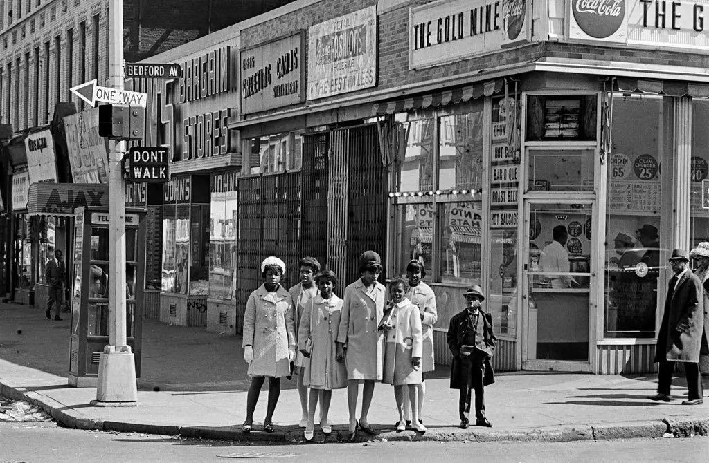 Bedford-Stuyvesant, Brooklyn (1967). Children wait to cross the street at Bedford Ave & Fulton St on Easter Sunday. Photographed by Don Hogan Charles.