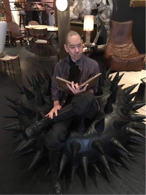 Portrait of the artist sitting on a big black spiky thing.