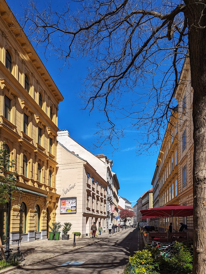 Josefstadt, Vienna. 3-4 storeys, no setbacks, mixed use, narrow streets, mixed in greenery, little parking, cars 'as guests'. Rows of tall casement windows, simple facade pattern, cheap plaster ornament, pastel colours. A slight curve in the street generates a sense of enclosure.