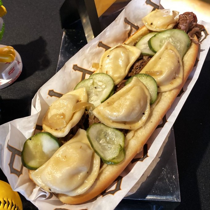 A foot-long hot dog and bun, topped with potato pierogis, pot roast, pickles and onions in a Pirates paper wrapper.