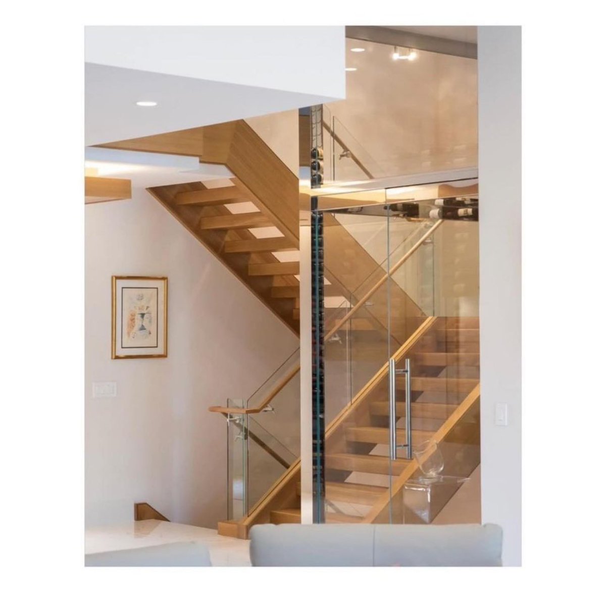 This dreamy mid-century modern staircase creates visual interest with a glass pocket design that is enhanced by natural oak and metal. We love how it’s flanked by the glass encased wine room. #Architecture #MidCenturyModern #CustomHome #DesignBuild #Michigan #JPCraig