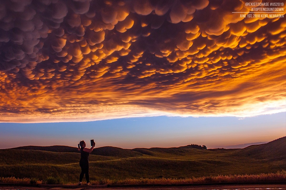 Exist2Chase's tweet photo. The wife taking a panorama on her iPad of an absolute stunner of a mammatus sunset near Kent, Nebraska back in 2018. What I really love about this image the most though is the sandhills baked in golden light post-storm. #newx #sunsets #exist2chase https://t.co/CiOUfcCxHS