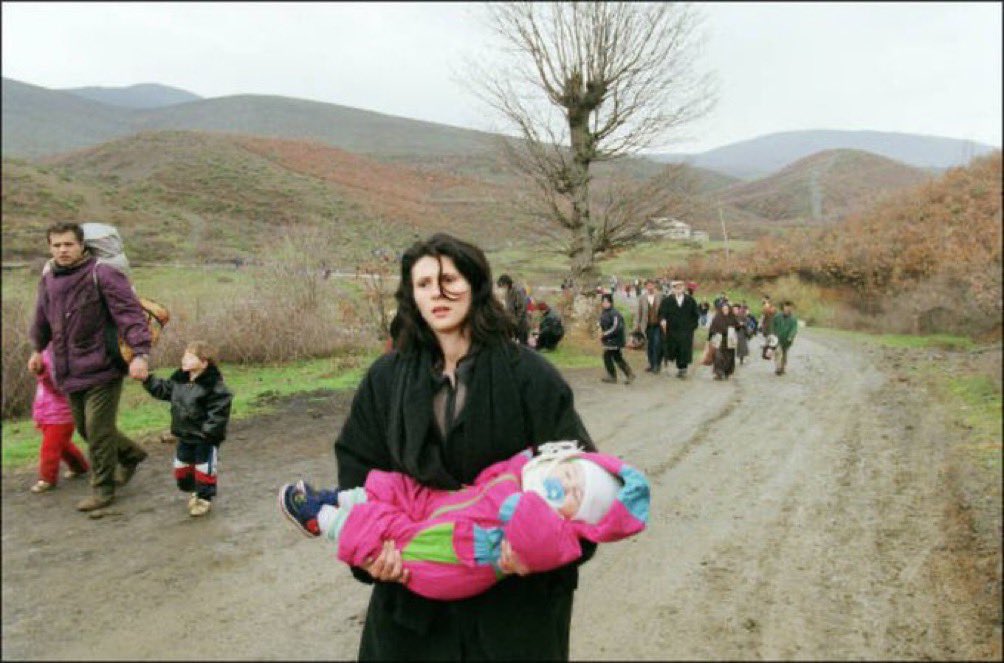 A woman carrying a baby arrives in Albania 03 April 1999 with fellow ethnic Albanian refugees fleeing Serb repression in Kosovo via the tiny border crossing of Pashtriku,north of Kukes. 𝘗𝘩𝘰𝘵𝘰 & 𝘊𝘢𝘱𝘵𝘪𝘰𝘯 𝘣𝘺 𝘑𝘰𝘦𝘭 𝘙𝘰𝘣𝘪𝘯𝘦/𝘈𝘍𝘗