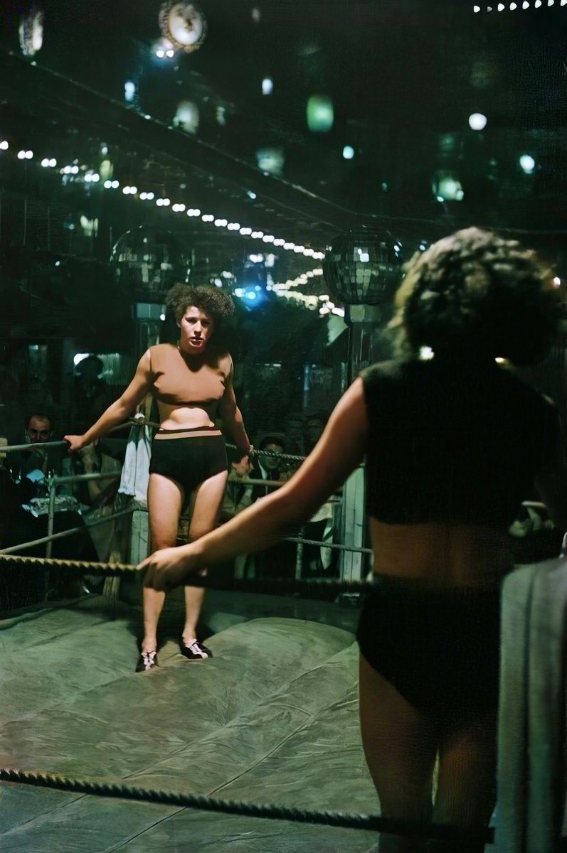 WOMEN'S WRESTLING IN THE NIGHTCLUB "JUNGMÜHLE" ON HAMBURG'S REEPERBAHN (1951)

Photographer Erich Lessing (Austria). This picture with the stare down of the two wrestlers before the match is our favourite, therefore we decided to try coloring it to bring it even more to life. Do