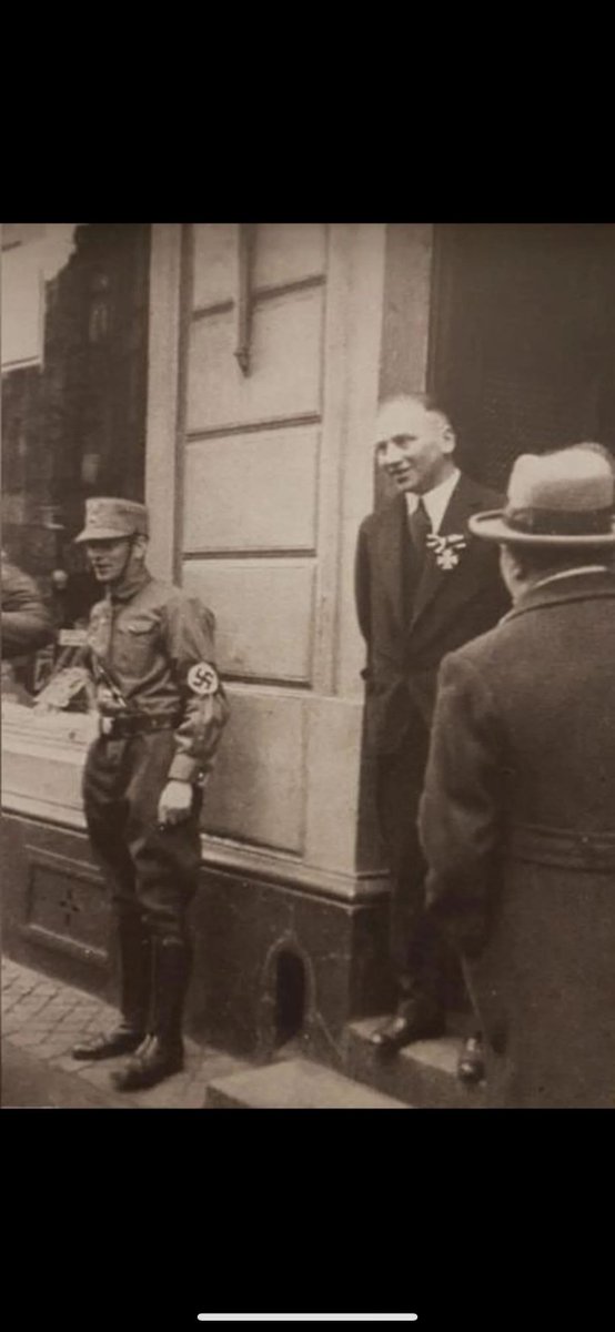 A German-Jewish WW1 veteran wears his Iron Cross while a Nazi soldier stands in front of his shop for intimidation, 1933