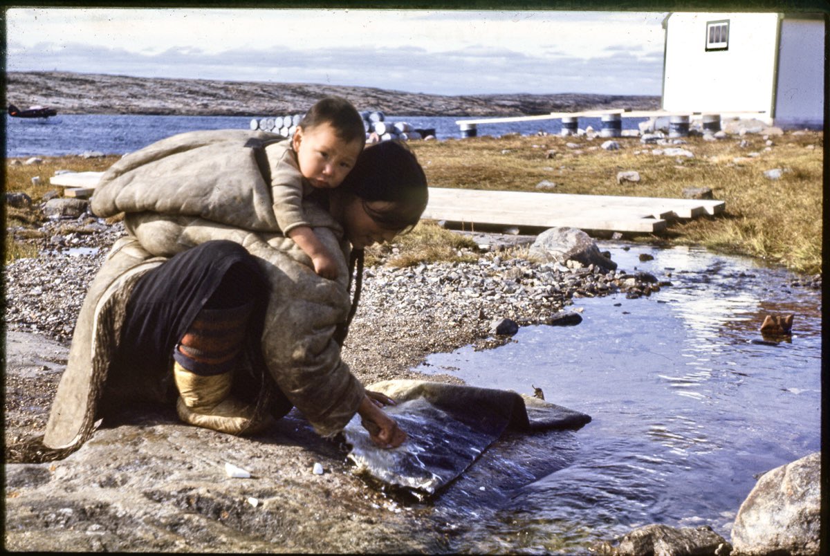 Woman in an amauti with infant, cleaning a seal skin in fresh water. Color slide photographed in 1947. Location listed as possibly Rankin Inlet or Arviat. 📷 Thomas Paterson | maa University of Cambridge