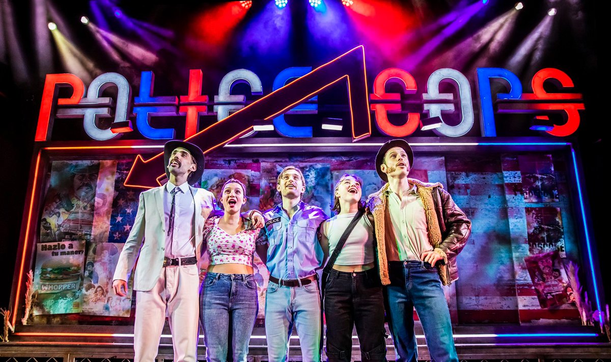 The cast of POLICE COPS: THE MUSICAL onstage singing and hugging, with a giant red, white and blue sign in the background reading POLICE COPS.