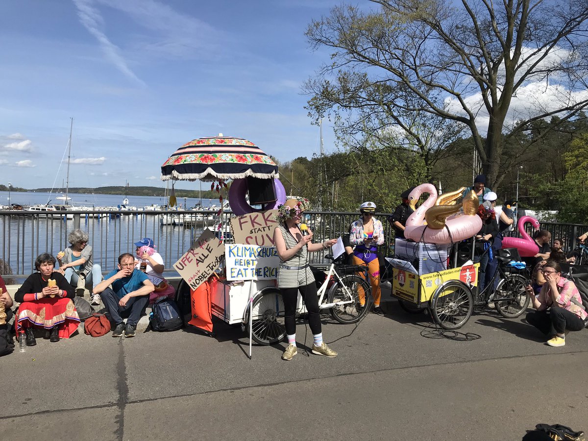 Die Satiredemo von @myGruni ist jetzt an der Brücke zur Insel Schwanenwerder angekommen. Eine Rednerin erzählt über die Geschichte des nahen Strandbads Wannsee & dem Konflikt mit den Bewohner:innen der Villen. Ein Redner begrüßt alle “zur allerersten Demo” der Insel