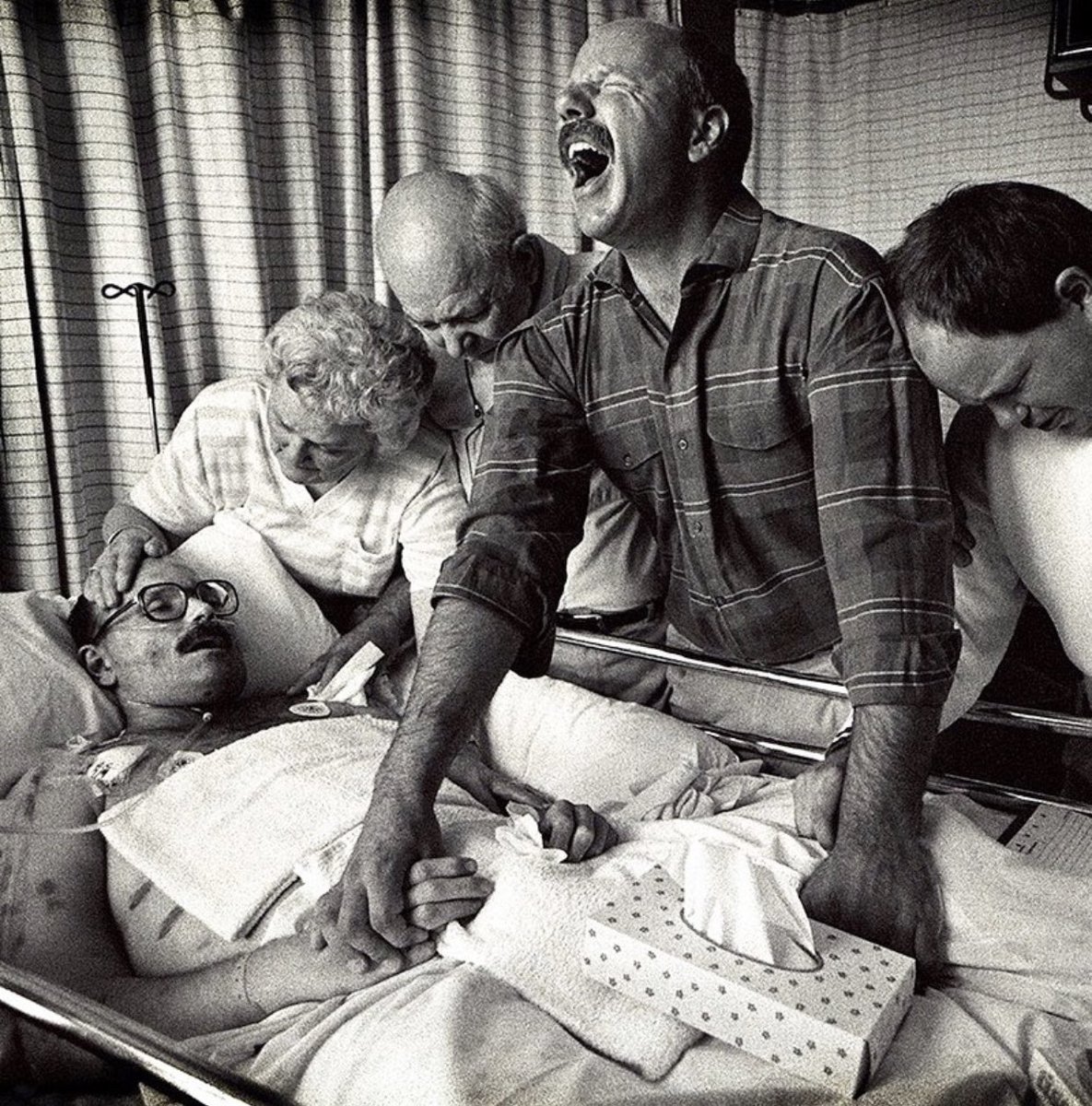 Captured in 1989 by Michael Schwarz, this photograph depicts 33-year-old Tom Fox during his final moments before he died from AIDS. He was surrounded by his family at Sacred Heart Hospital in Eugene, Oregon.