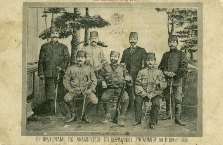 1908 devriminin önde gelen kişilerini resmeden Fransızca, Rumca Osmanlıca kartpostal. Ön solda oturan Ohrili Eyüp Sabri Akgöl.