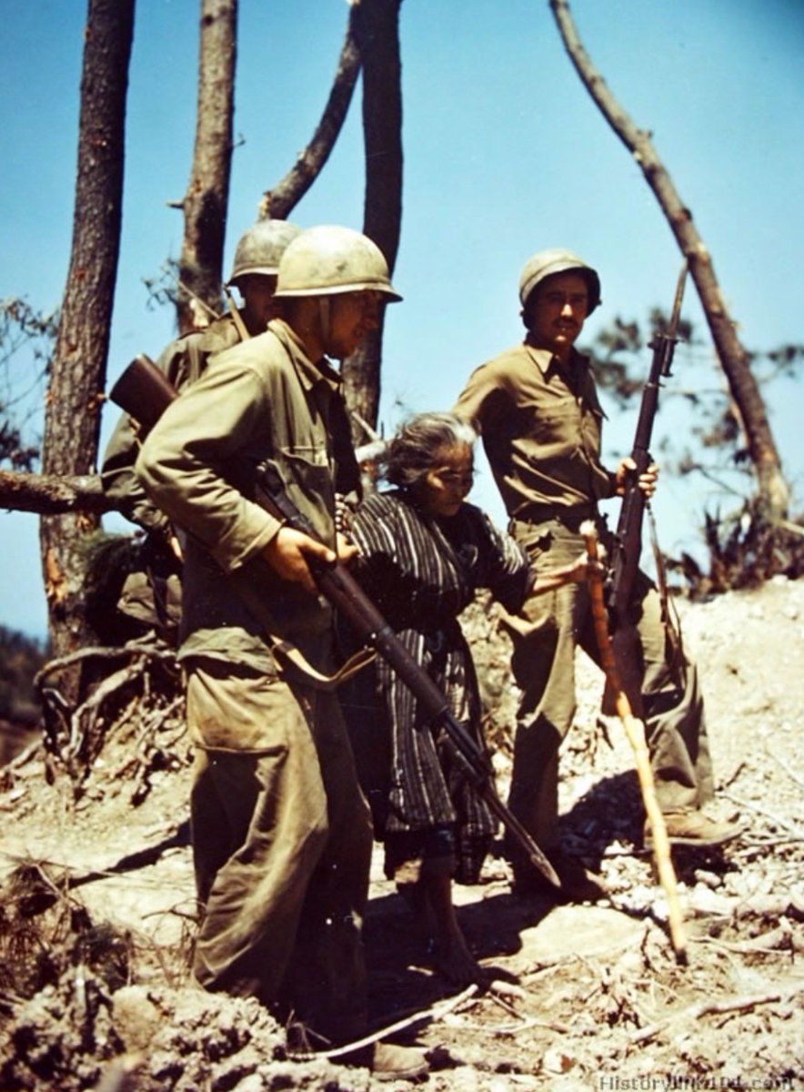 In 1945, American soldiers help an Okinawan woman away from the front lines, during the Battle of Okinawa. 🪖