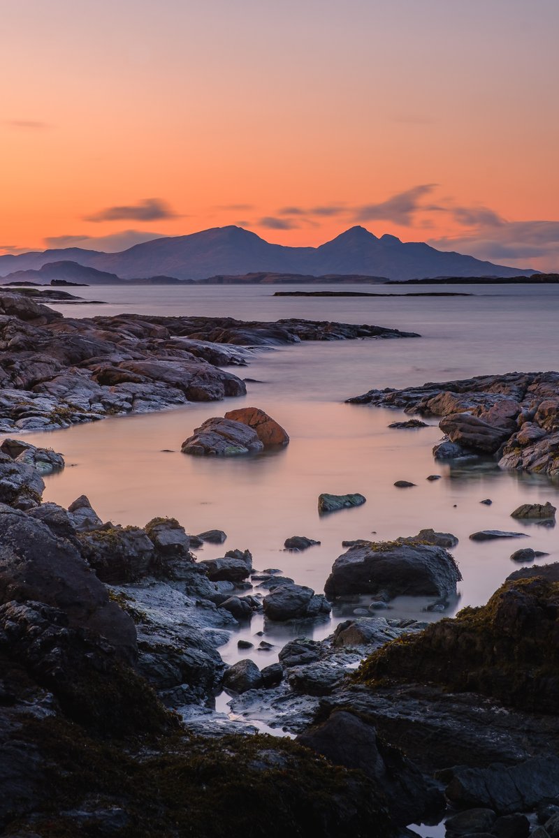 Primordial I - Inbhir Allt na Luachair, Portuairk, #Ardnamurchan The rugged peaks of the Rùm Cuillin silhouetted against the orange of a dusk sky, viewed immediately after sunset from amongst the rocky shoreline of Inbhir Allt na Luachair.