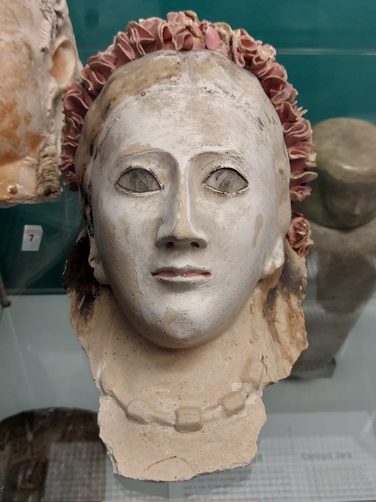 Mummy mask of a woman, wearing a wreath of pink flower petals and a necklace. Painted plaster, eyes inlaid with glass. From Middle #Egypt. #Roman Period, late 1st - early 2nd century AD.  On display at Museum August Kestner, Hannover.