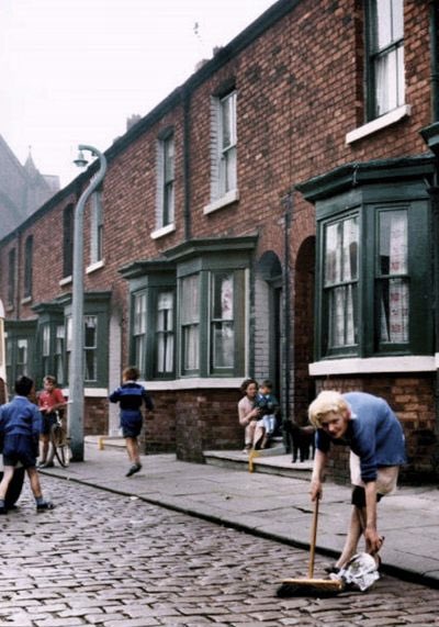 Mrs Marion Taylor of no. 8 Archie Street, Salford, sweeps up the rubbish from her section of the street. On the step of no. 12 is Mrs Chapman with son Keith. April, 1962.